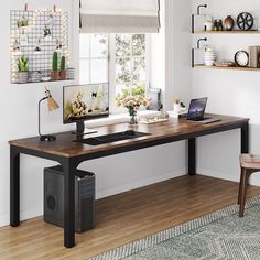 a desk with a computer on top of it in front of a window and shelves