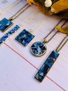 four necklaces with different designs on them sitting on top of a wooden table next to flowers