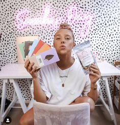 a person sitting on a chair holding up some books and looking at the camera with one hand