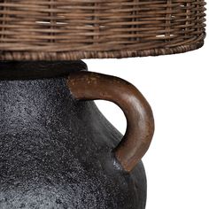 a brown basket sitting on top of a table next to a black vase with a wooden handle