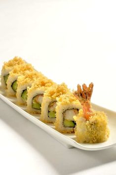 a white plate topped with sushi covered in cheese and cucumber crumbs