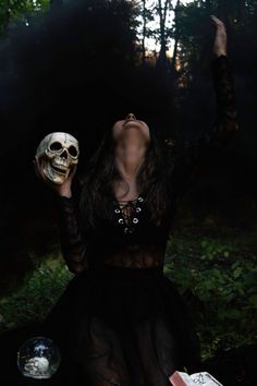 a woman in a black dress holding a skull mask and looking up into the sky