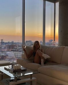 a woman sitting on top of a couch in front of a window next to a coffee table