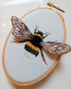 a small embroidered bee sitting on top of a wooden hoop with gold and black accents