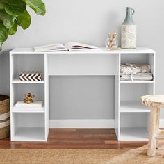 a white shelf with books and other items on it next to a potted plant