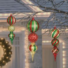 three christmas ornaments hanging from a tree in front of a house with lights on it