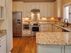 a kitchen with white cabinets and granite counter tops, stainless steel appliances and wood flooring