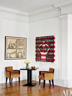 two chairs and a table in a white room with artwork on the wall behind them