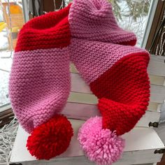 a pink and red knitted scarf sitting on top of a stack of books next to a window