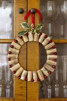 a wine cork wreath is hung on a door with red ribbon and holly berry decorations