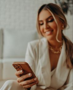 a woman sitting on a couch holding a cell phone in her hand and smiling at the camera