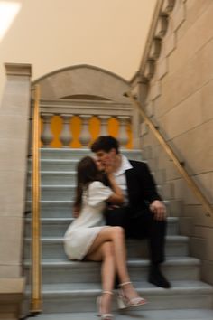 a man and woman are sitting on the stairs kissing in front of an entrance to a building