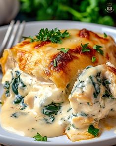 a white plate topped with lasagna covered in sauce and spinach leaves next to a fork