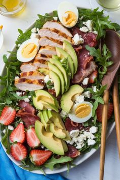 a salad with meat, avocado, strawberries and hard boiled eggs on it