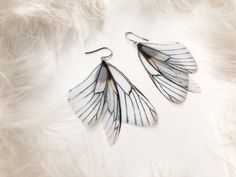 two pairs of white and black earrings on top of a feathery surface with one pair dangling