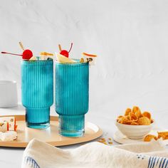 two blue glass cups sitting on top of a table next to a bowl of food