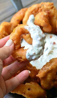 a hand holding a fried onion rings with ranch dip