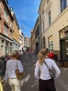 two women are walking down the street in front of some buildings with bicycles parked on the sidewalk