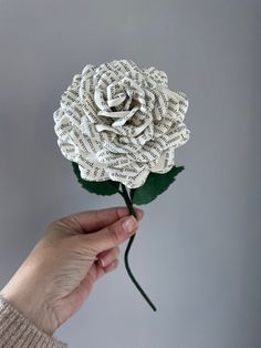 a hand holding a paper rose made out of old book pages in front of a gray background