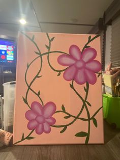 a pink painting with flowers on it sitting on a table next to a remote control