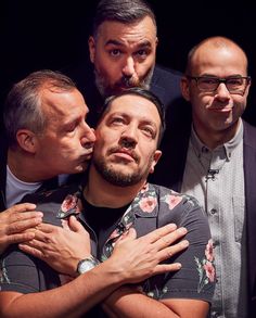 three men are hugging each other while one man is wearing glasses and the other has a beard