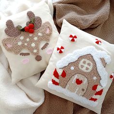 two decorative pillows on a bed covered in white and brown blankets, one with a reindeer design