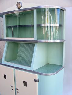 an old fashioned display cabinet with glass doors and metal trim on the bottom, in front of a white wall