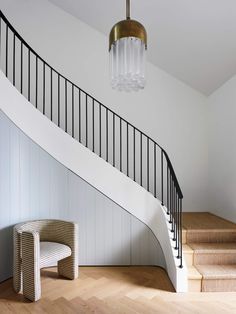 a white staircase with a chandelier hanging from the ceiling next to a wooden floor