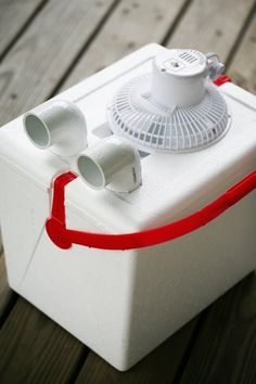 an ice chest with two cups and a fan attached to the lid, sitting on a wooden deck