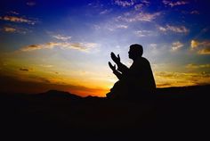 the silhouette of a man sitting in front of a sunset with his hands clasped to each other