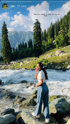 a woman standing on top of a rock next to a river