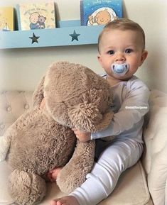 a baby sitting on a couch with a teddy bear and pacifier in his mouth