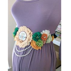 a purple dress with flowers and pearls on the belt is displayed in front of a mannequin