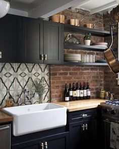 a kitchen with black cabinets, white sink and wooden counter tops in front of a brick wall