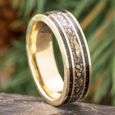 a wedding ring with gold and black inlays sitting on top of a rock