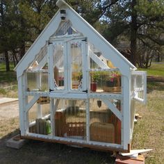 a small white house made out of pallet wood and glass windows with plants growing inside