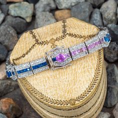 This beautiful one link style hinged bracelet featuring multi-colored natural sapphires in the center of each link. There are five (5) oval sapphires in four-prong settings set equidistant throughout the length of the bracelet. There are also sixty-two (62) natural sapphires that are princess cut and are channel set centered in the middle of each link. Accenting each link are bead set diamonds above and below the settings of sapphires. The bracelet measures 9.2 mm at the widest points and rises 5.1mm from the wrist with a total length of 6.5 inches and has a slide lock clasp and two (2) figure eight safety clasps. It fits up to a 6.5 inch wrist. Multi-stone Round Diamond Bracelet For Anniversary, Oval Sapphire Tennis Bracelet With 17 Jewels, Elegant Multi-stone Oval Tennis Bracelet, Formal Multi-stone Cubic Zirconia Tennis Bracelet, Platinum Sapphire Multi-stone Jewelry, Elegant Oval Multi-stone Tennis Bracelet, Exquisite Multi-stone Platinum Jewelry, Elegant Multi-stone Sapphire Bracelet, Elegant Sapphire Multi-stone Bracelet