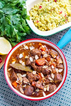 a bowl filled with meat and vegetables next to other food on a blue table cloth