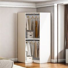 a white closet with clothes hanging on the door and drawers in it, next to a bed