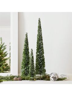 three small trees sitting on top of a table next to a mirror and christmas decorations