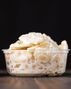 a plastic bowl filled with bananas on top of a wooden table next to a black background