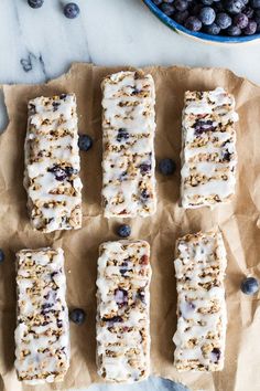 blueberry granola bars are lined up on parchment paper next to a bowl of blueberries