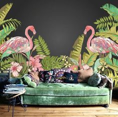 a green couch sitting in front of a wall with pink flamingos and tropical leaves on it