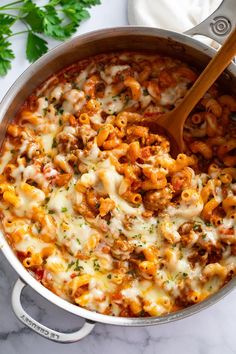 a large pot filled with pasta and cheese on top of a counter next to a wooden spoon