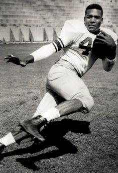 an old photo of a football player running with the ball in his right hand and one foot on the ground