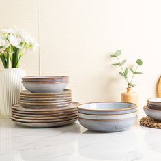 there are many bowls on the table with flowers in vases next to each other