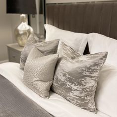 the pillows are lined up on the bed with white sheets and gray linens,