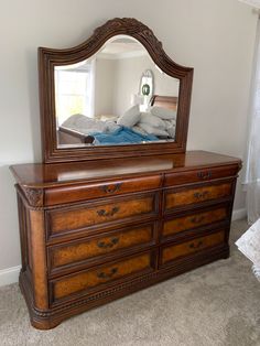 a dresser with a mirror on top of it in front of a bed and window