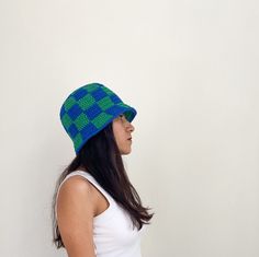 a woman wearing a blue and green knitted hat with squares on the front, standing against a white wall