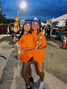 two women in orange shirts holding donuts and drinking sodas while standing next to each other